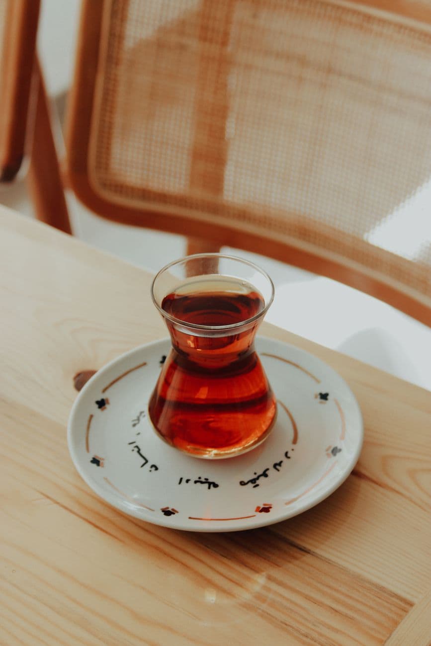 A glass of Turkish tea in a traditional tulip-shaped glass resting on a decorative saucer.