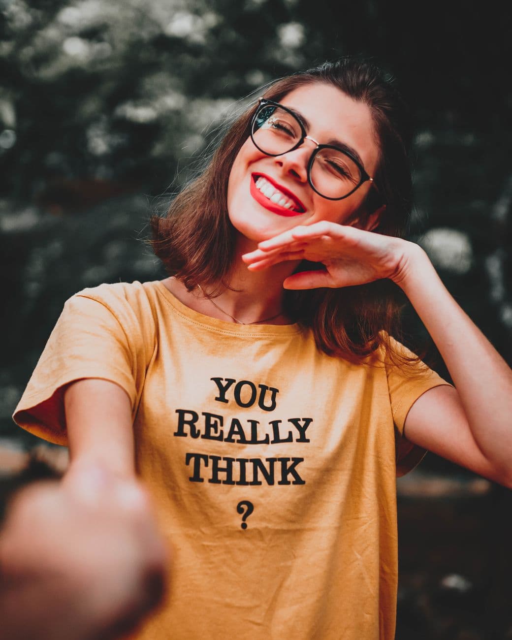 Cheerful woman with glasses smiling while posing outdoors in a yellow t-shirt.