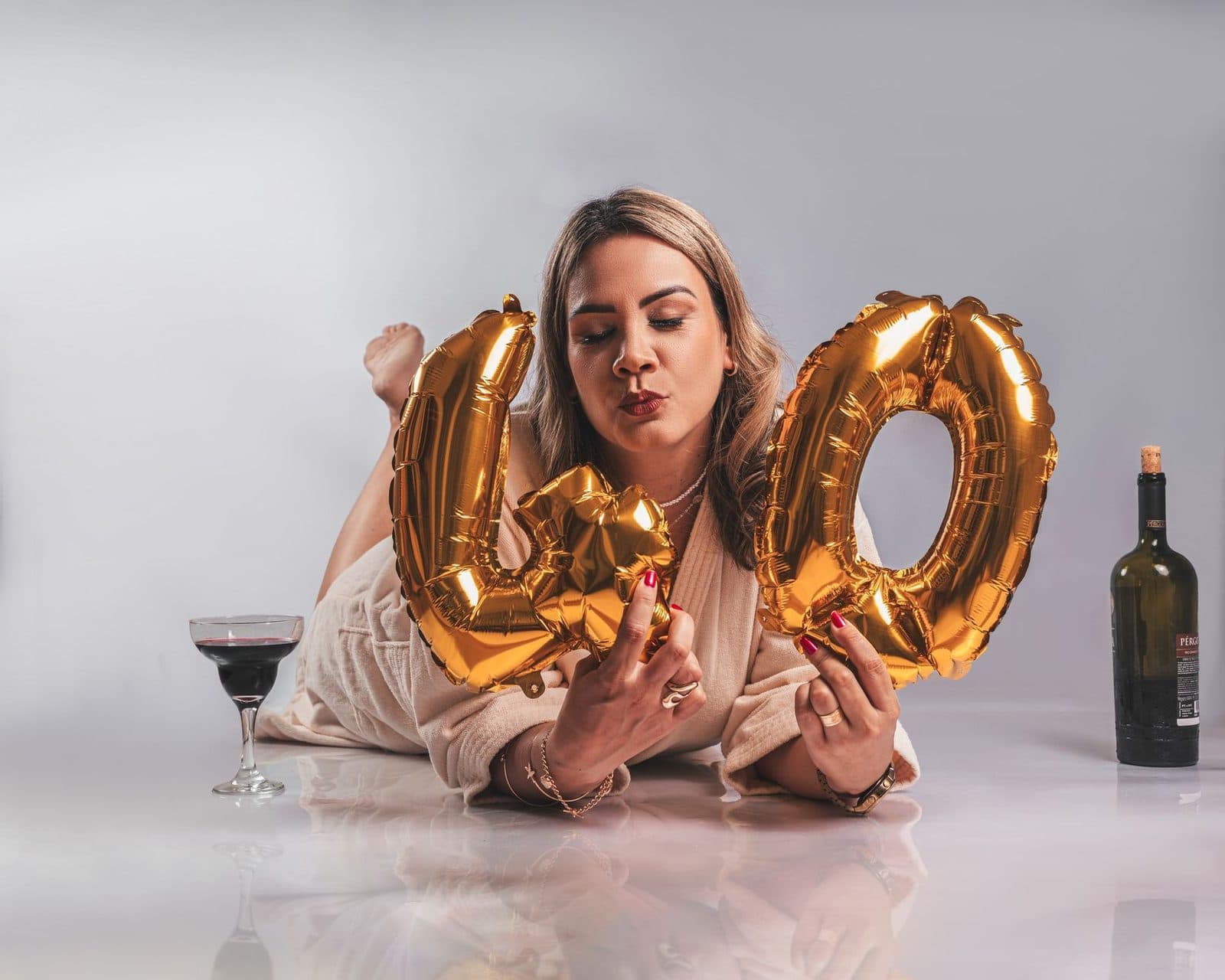 Woman celebrating her 40th birthday with golden balloons and a glass of wine.