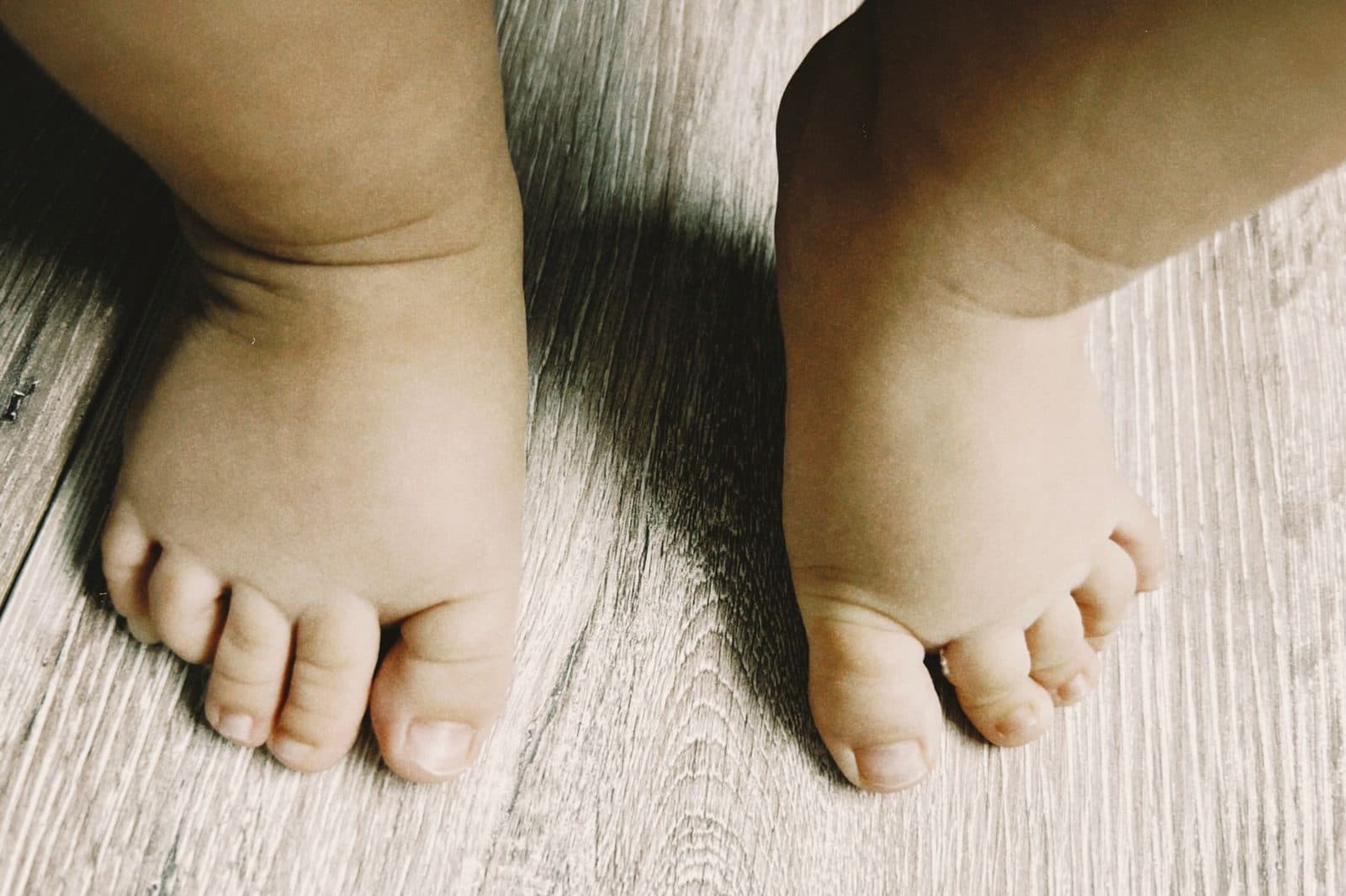 Close-up of baby feet standing on a wooden floor, capturing innocence and charm.