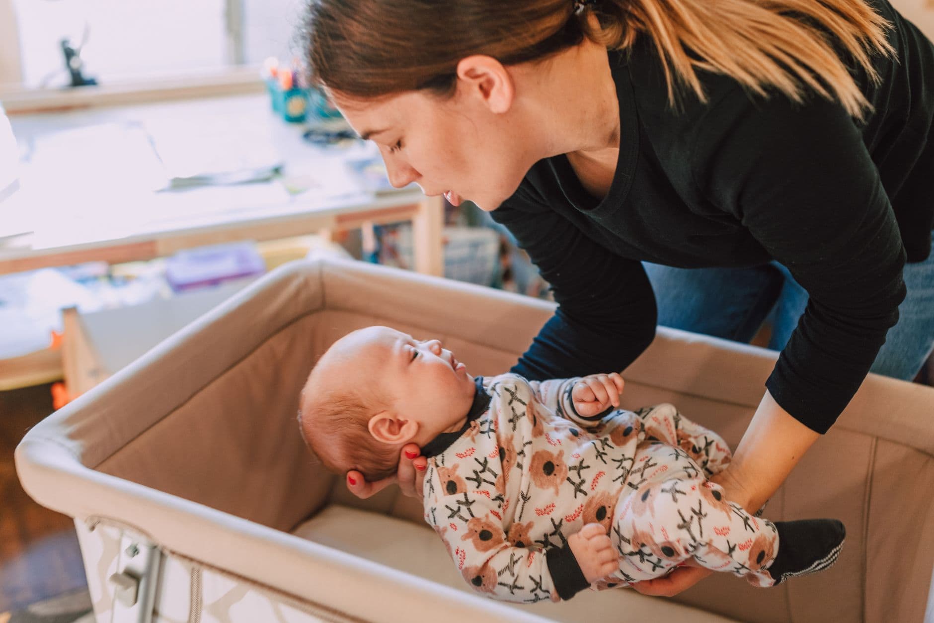 A mother lovingly interacts with her baby in a cozy nursery setting, emphasizing parental affection.