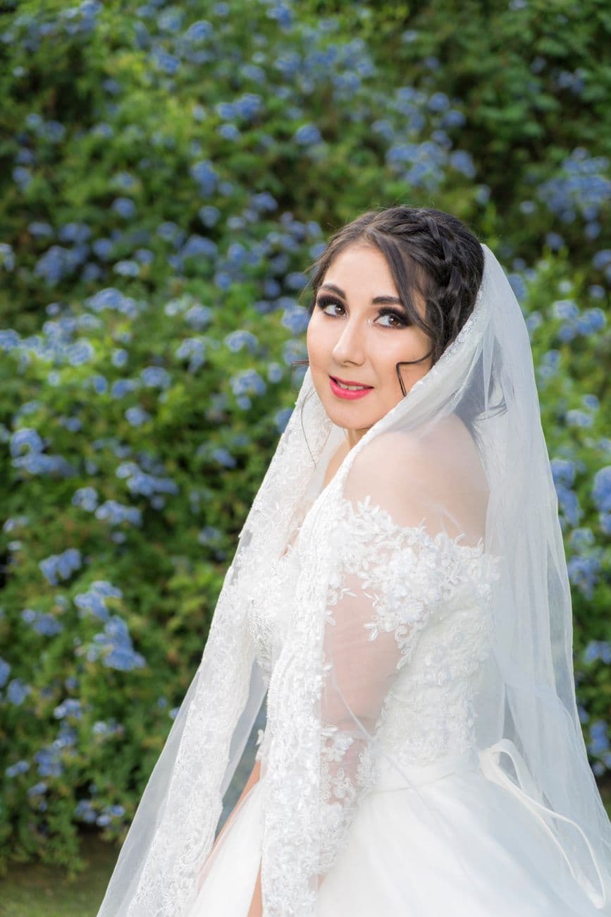 Bride outdoors in a lace dress with veil surrounded by beautiful flowers.