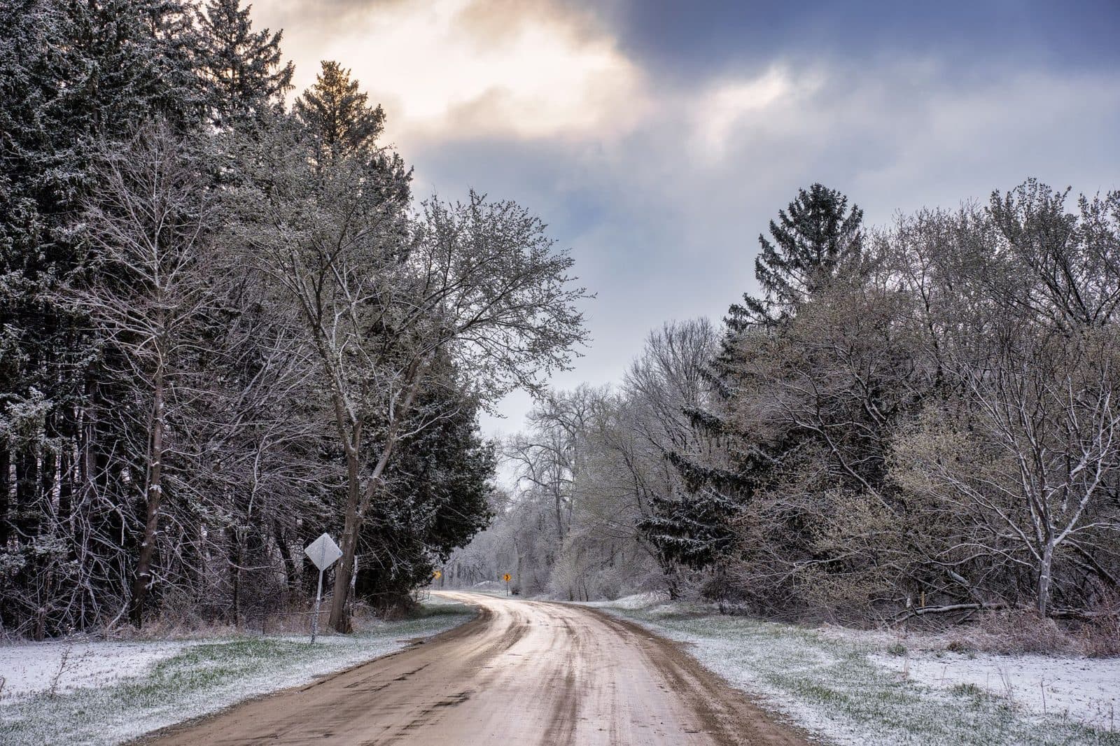 Discover the tranquility of a snow-covered country road winding through a serene winter forest.