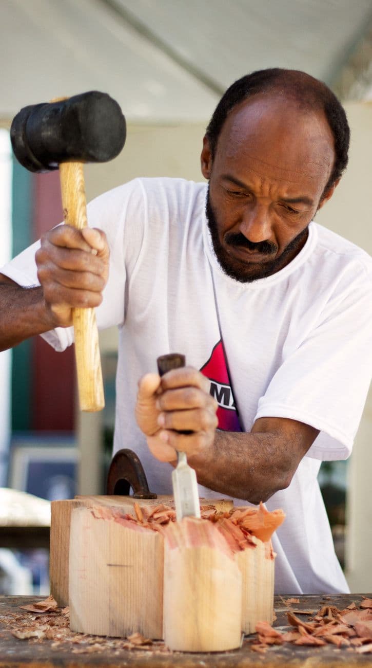 A craftsman focused on wood carving with a chisel and mallet, showcasing precise woodworking skills.