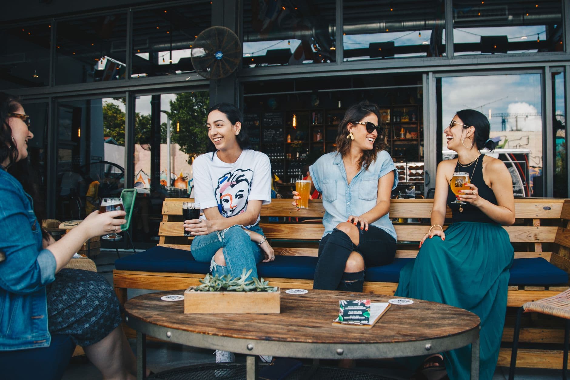 Women friends smiling and relaxing with drinks at an outdoor bar.